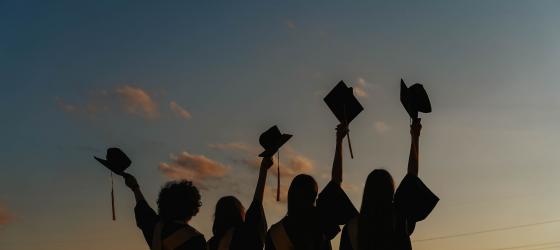 immagine sfuocata di gruppo studenti di spalle con toga che alzano al cielo cappello laurea
