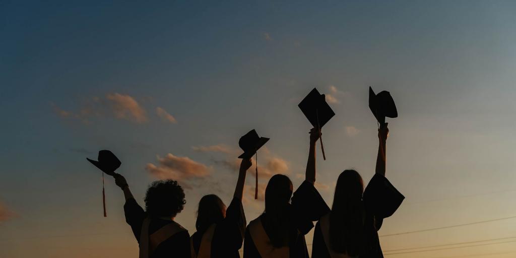 immagine sfuocata di gruppo studenti di spalle con toga che alzano al cielo cappello laurea